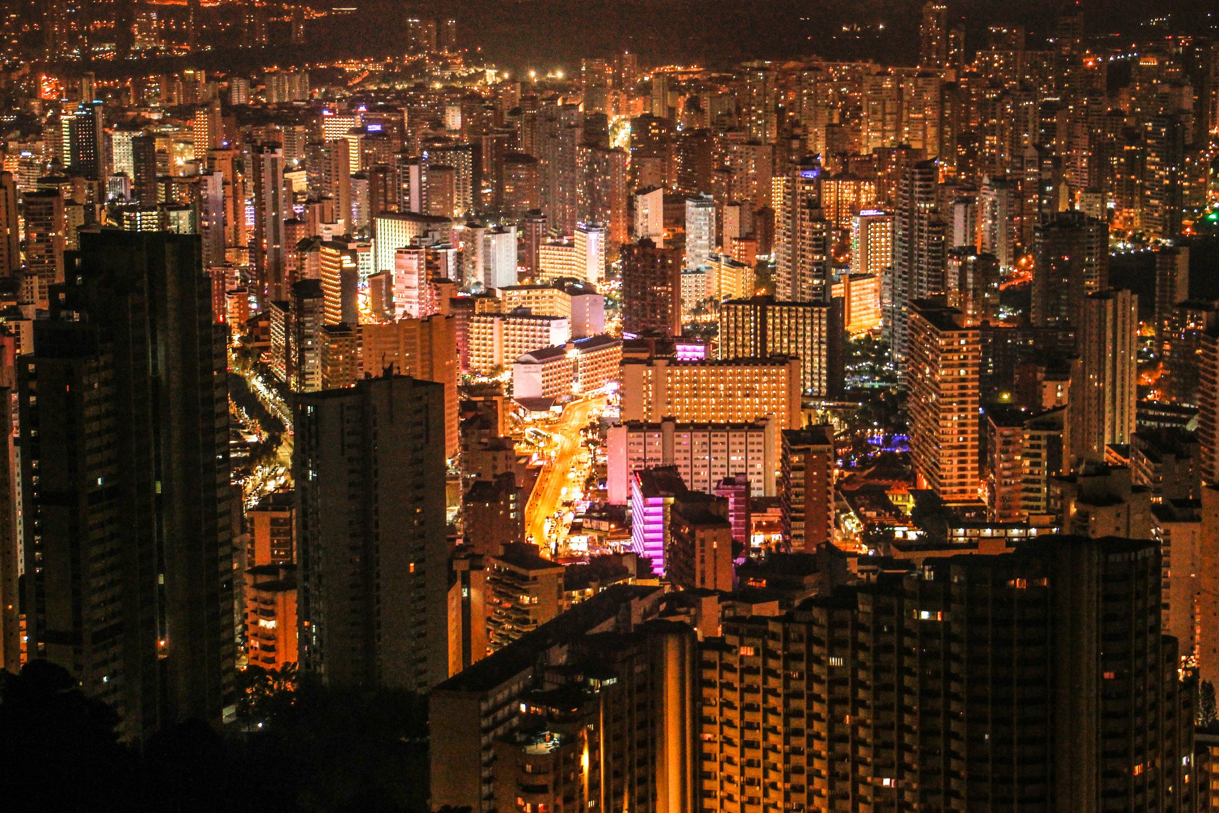 Nighttime cityscape of a densely packed urban area with illuminated high-rise buildings and streets.