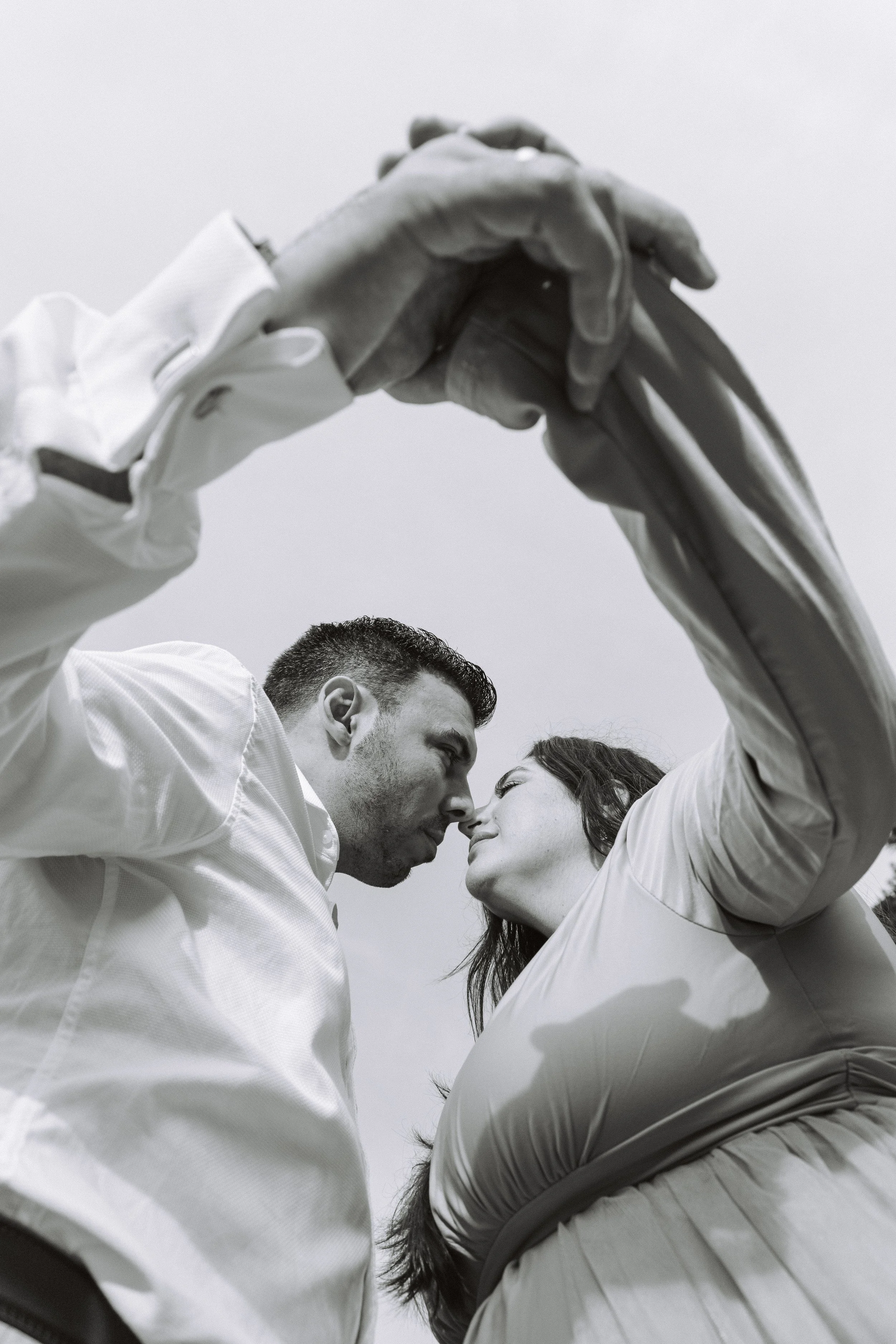 A black and white photo of a couple standing close, with their foreheads touching and eyes closed, under an umbrella held by one of them.
