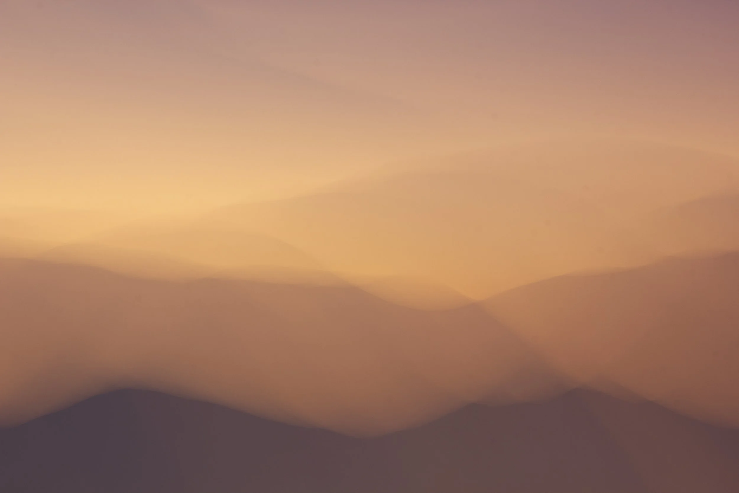 Blurred silhouette of mountains against a pastel-colored sky at sunset or sunrise.