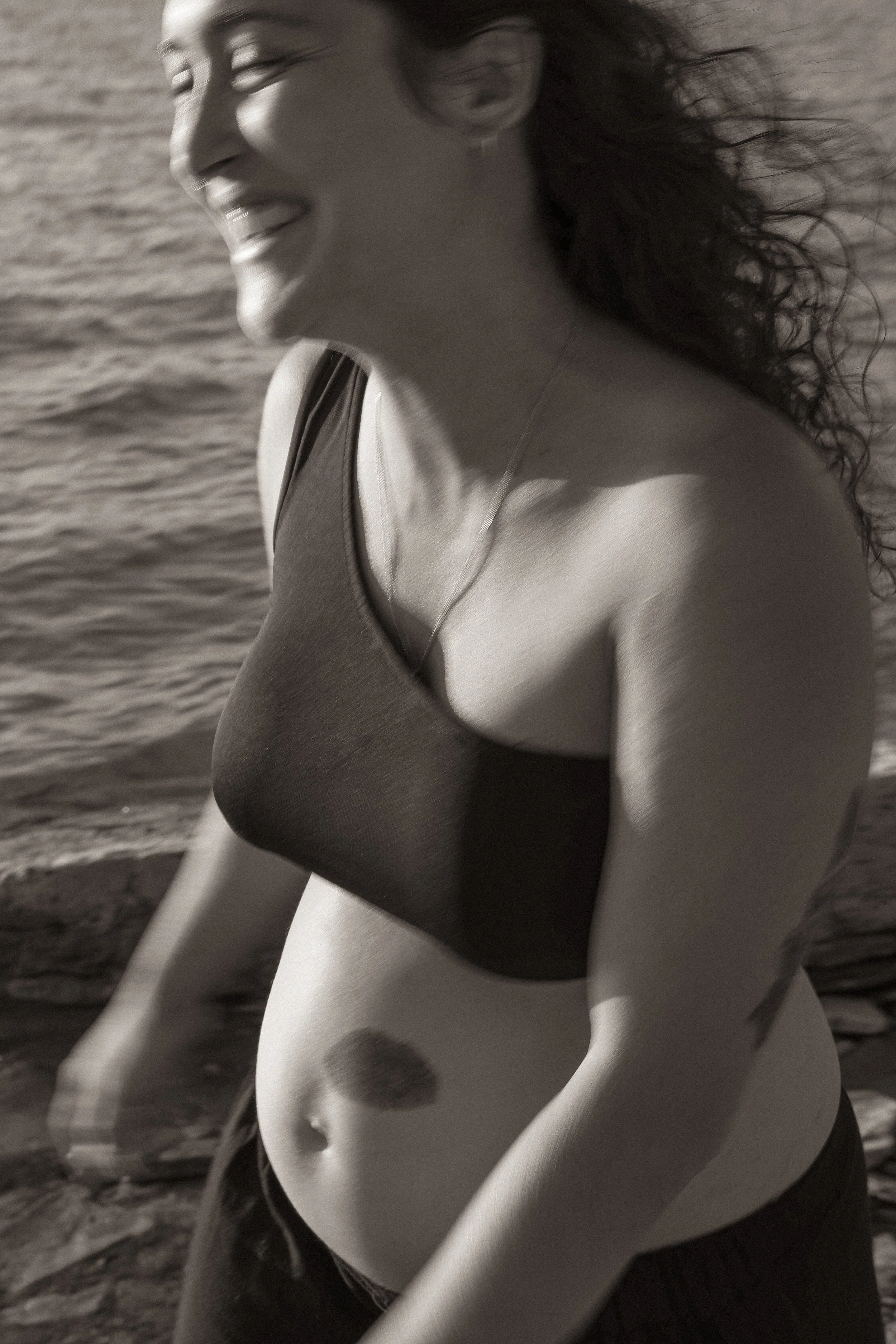 A cinematic scene of a woman smiling while running near the ocean, wearing a black sports bra and shorts, with wind blowing her hair.