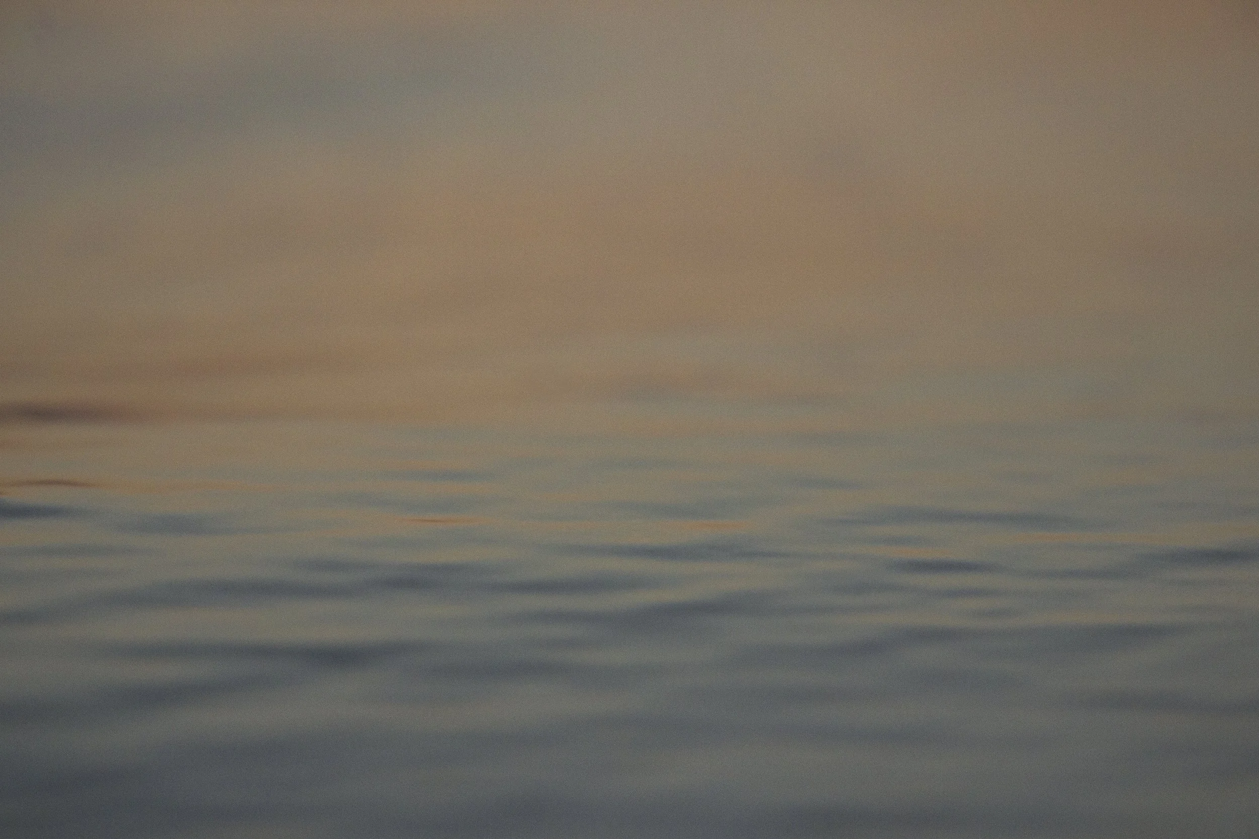 Calm ocean water with gentle ripples and a soft pinkish-orange sunset sky reflection.