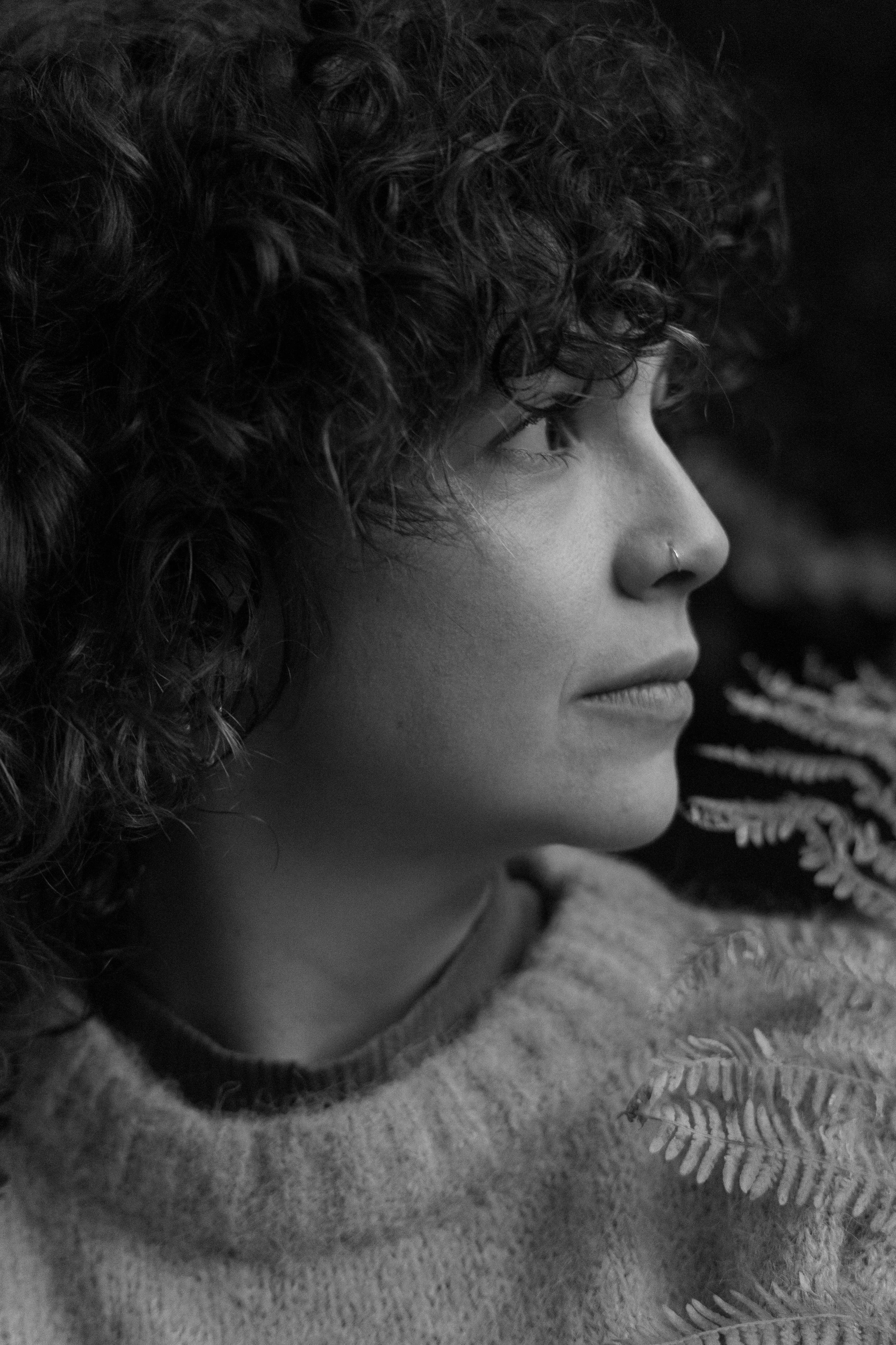 A portrait of woman with curly hair and a nose ring gazing to the side in black and white.