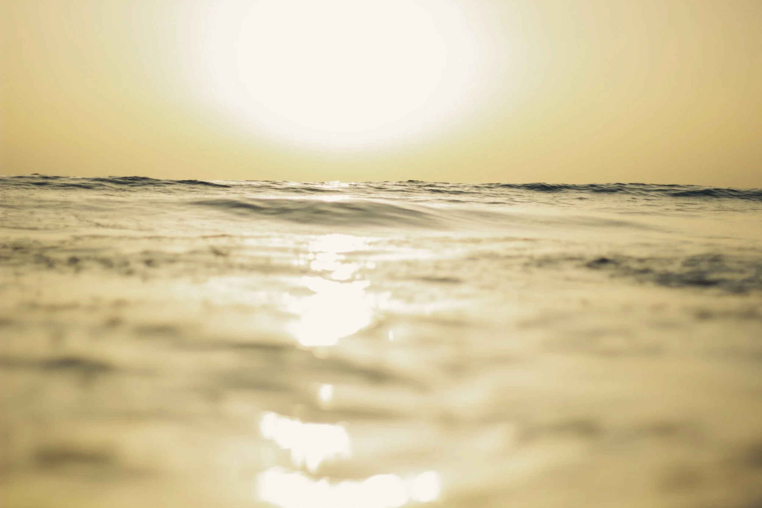 Sunset over calm ocean water with gentle waves, sunlight reflecting on the surface.