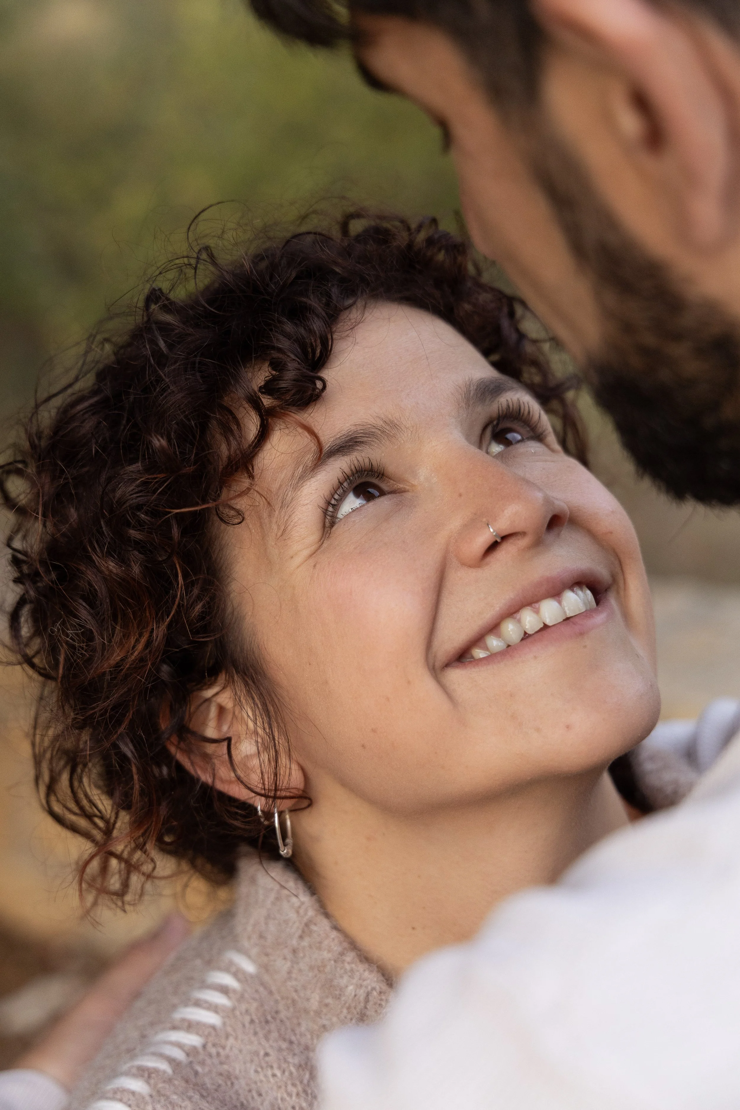 Close-up of a woman with curly hair smiling and looking up at a man, with a soft background.