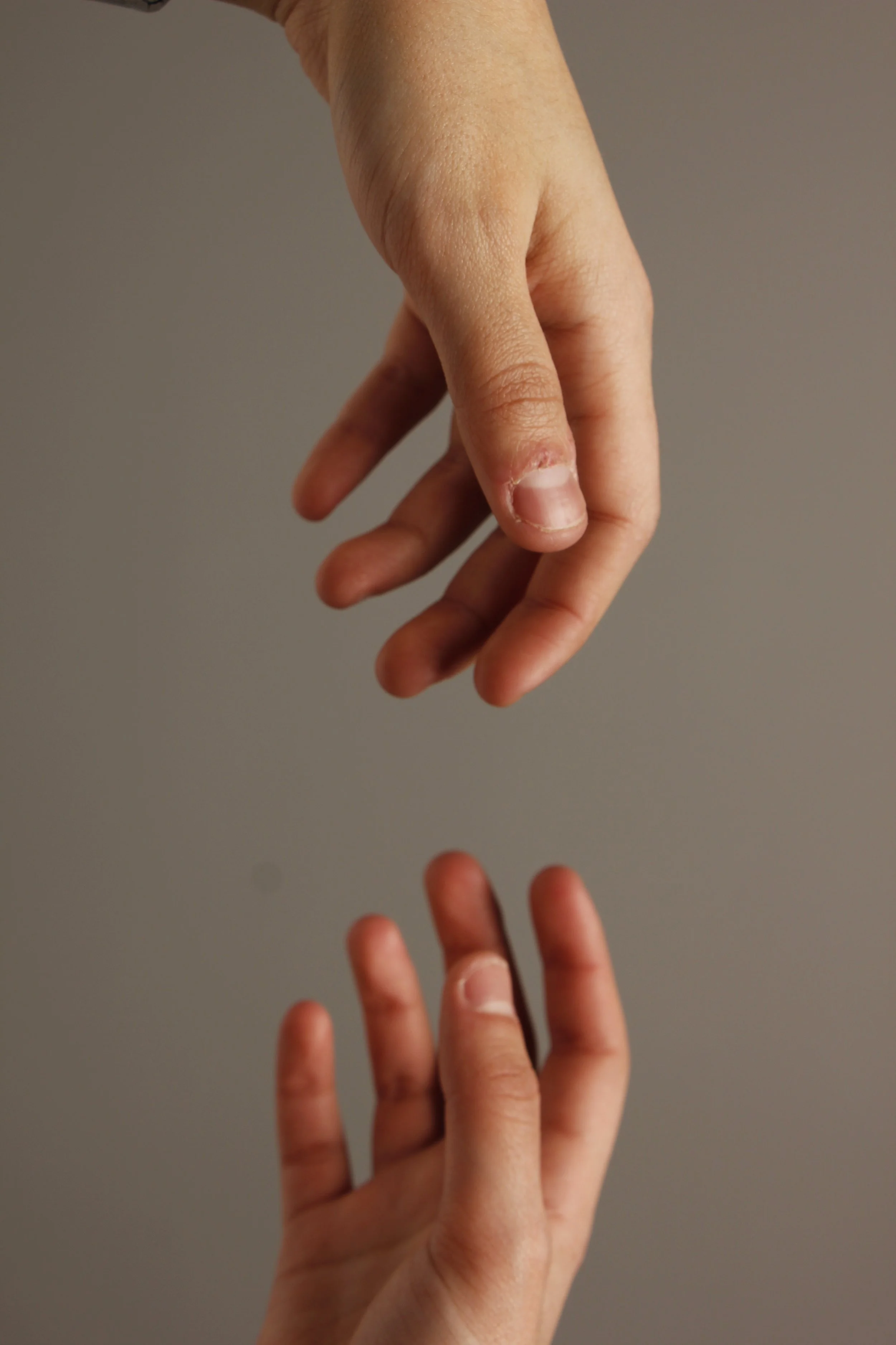 Two hands reaching toward each other, one with fingers slightly curled downward, against a plain background.
