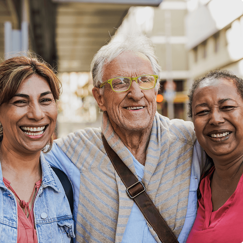 Three friends smiling and standing close together outdoors.