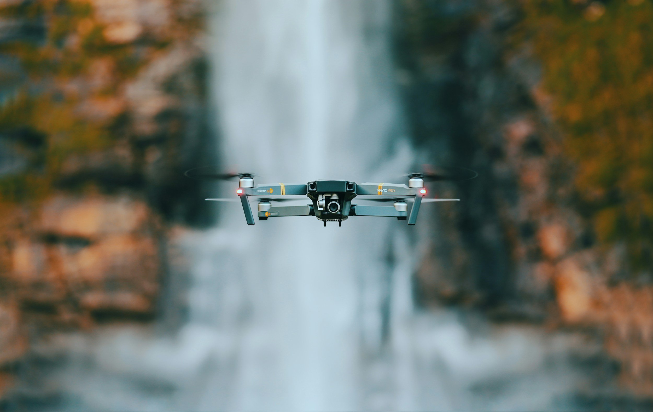 A drone flying over a waterfall with rocky cliffs on either side.