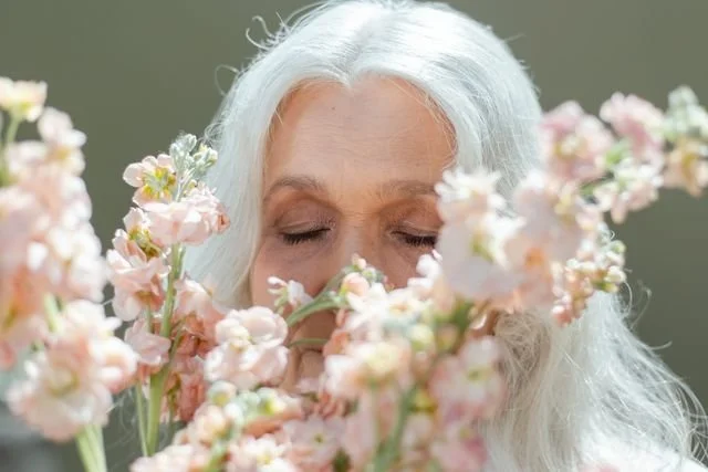 older woman with eyes closed face partly hidden by flowers