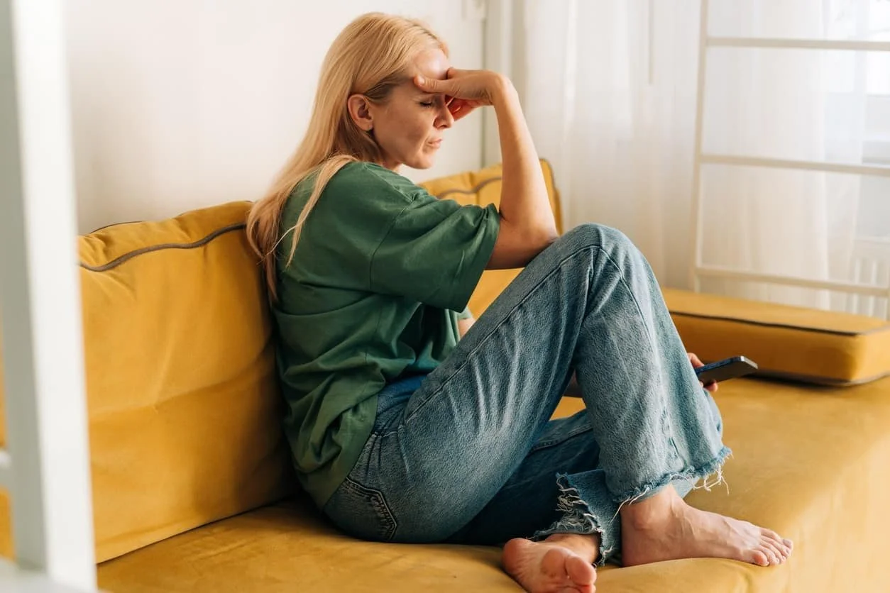 woman on yellow couch with head in hand