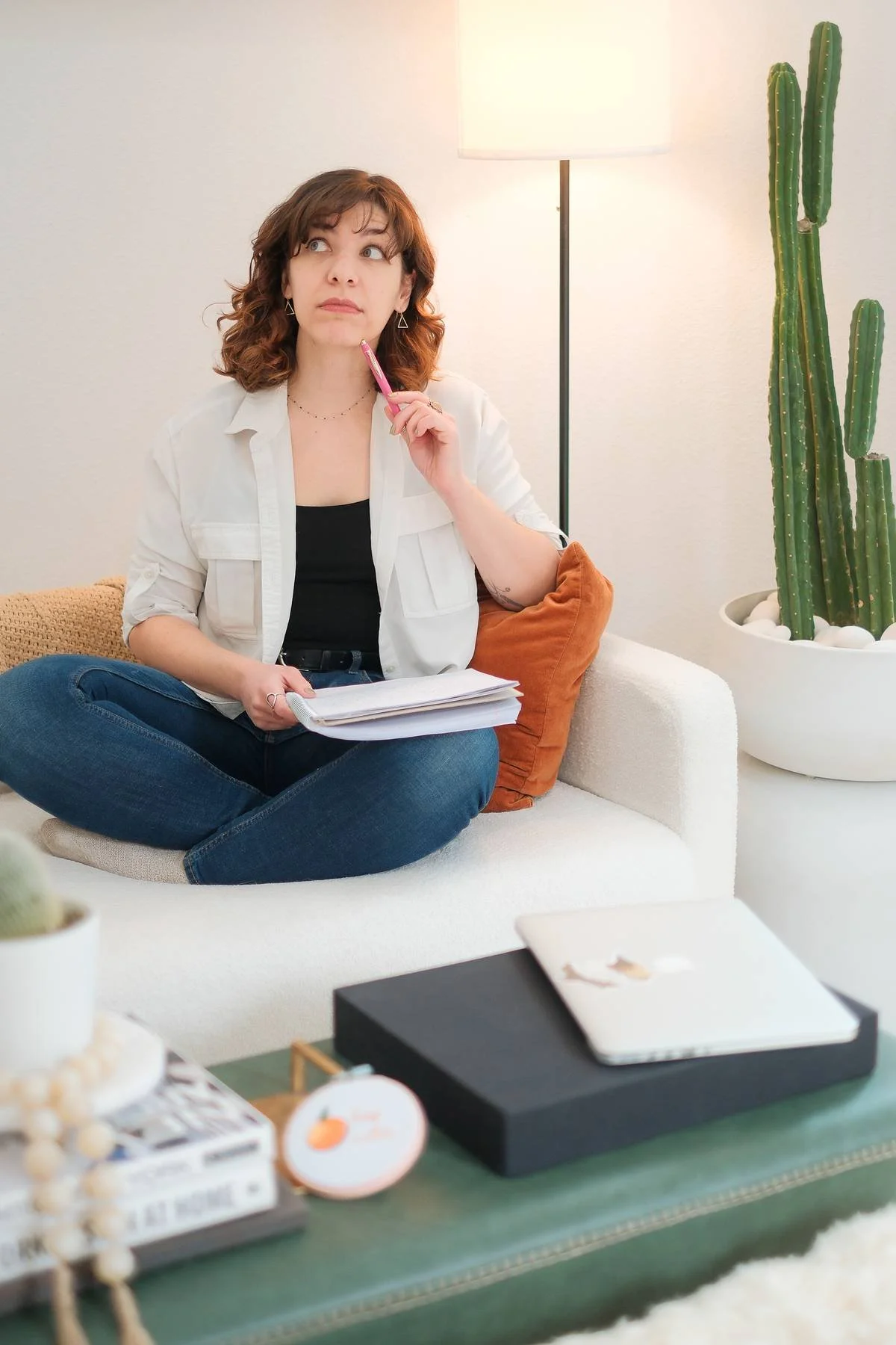 Rebecca, a Copywriter and Marketing Strategist, sitting on a couch, holding a pen to her face while deep in thought.