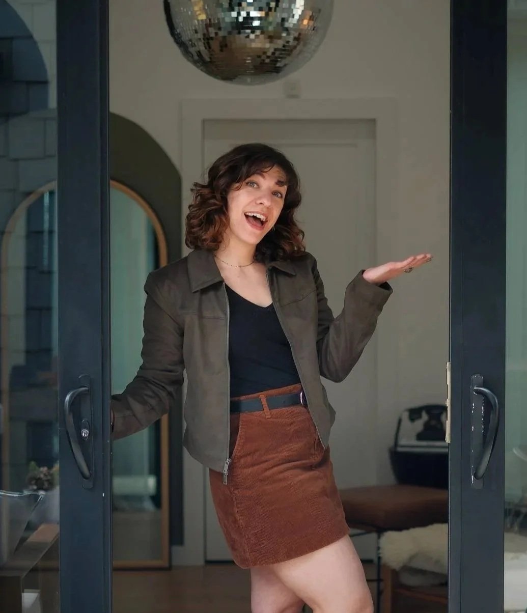 Copywriter Rebecca Brumberg standing in an open doorway, holding up her hand in a serving gesture.