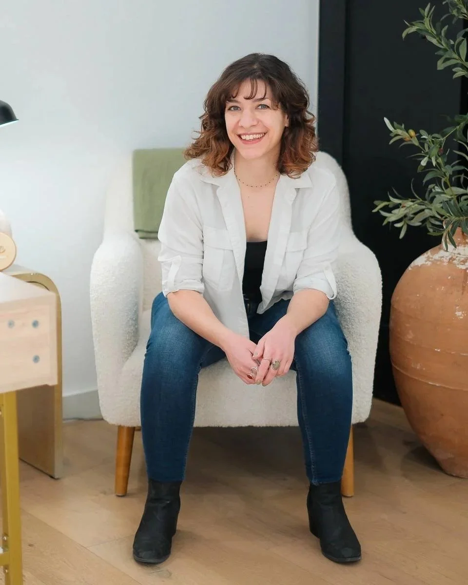 Copywriter Rebecca sitting on a chair, leaning forward with her arms resting on her legs, and smiling at the camera.