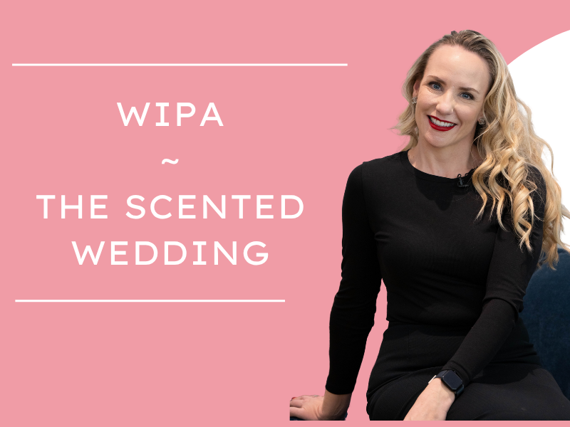A woman (Tiffany Rose Goodyear) with blonde hair, wearing a black dress, smiling, sitting on a chair against a pink background with white text that reads 'WIPA ~ THE SCENTED WEDDING'.