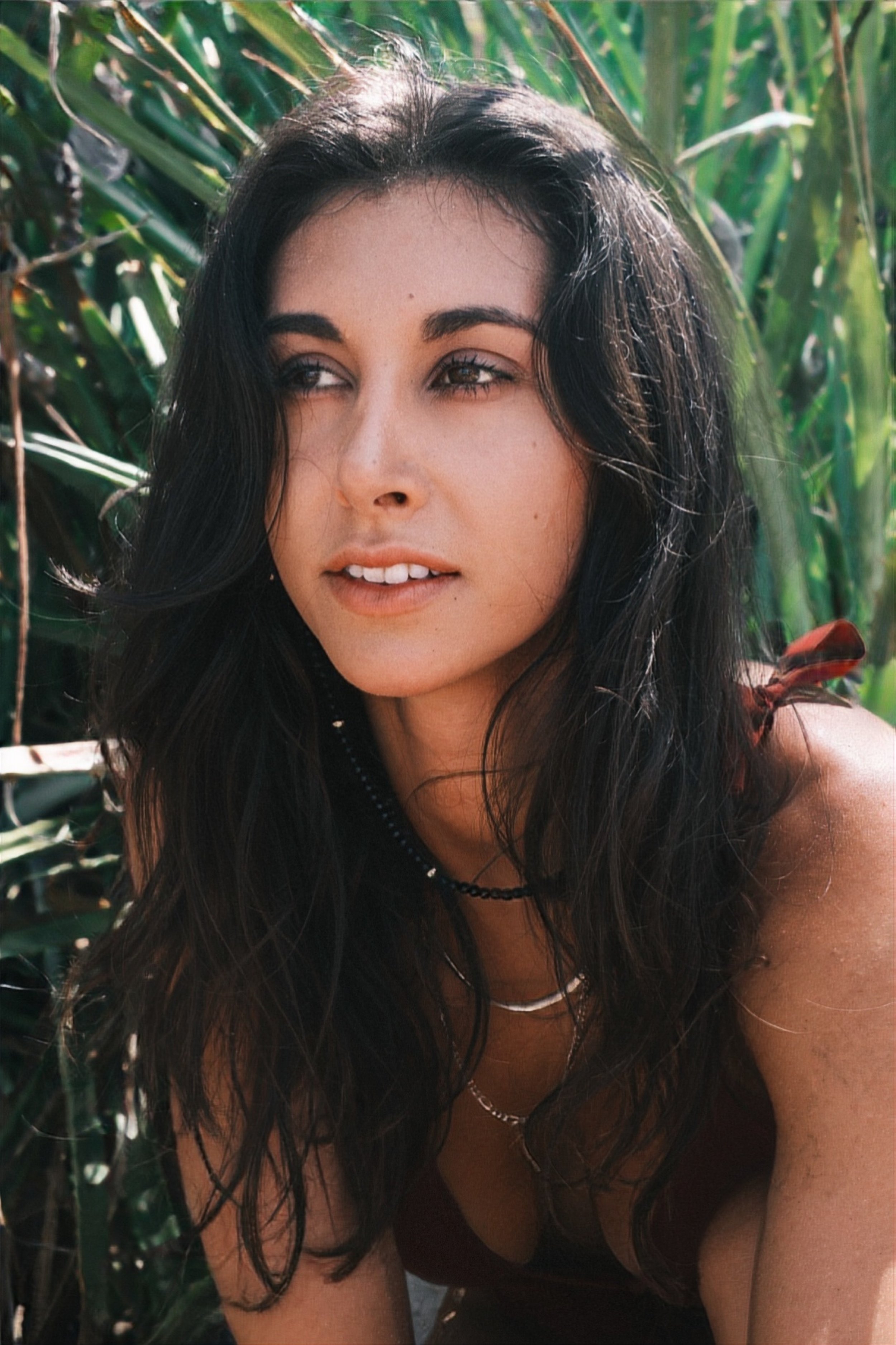 Woman meditating outdoors in a seated yoga pose with hands in prayer position, eyes closed, surrounded by greenery.