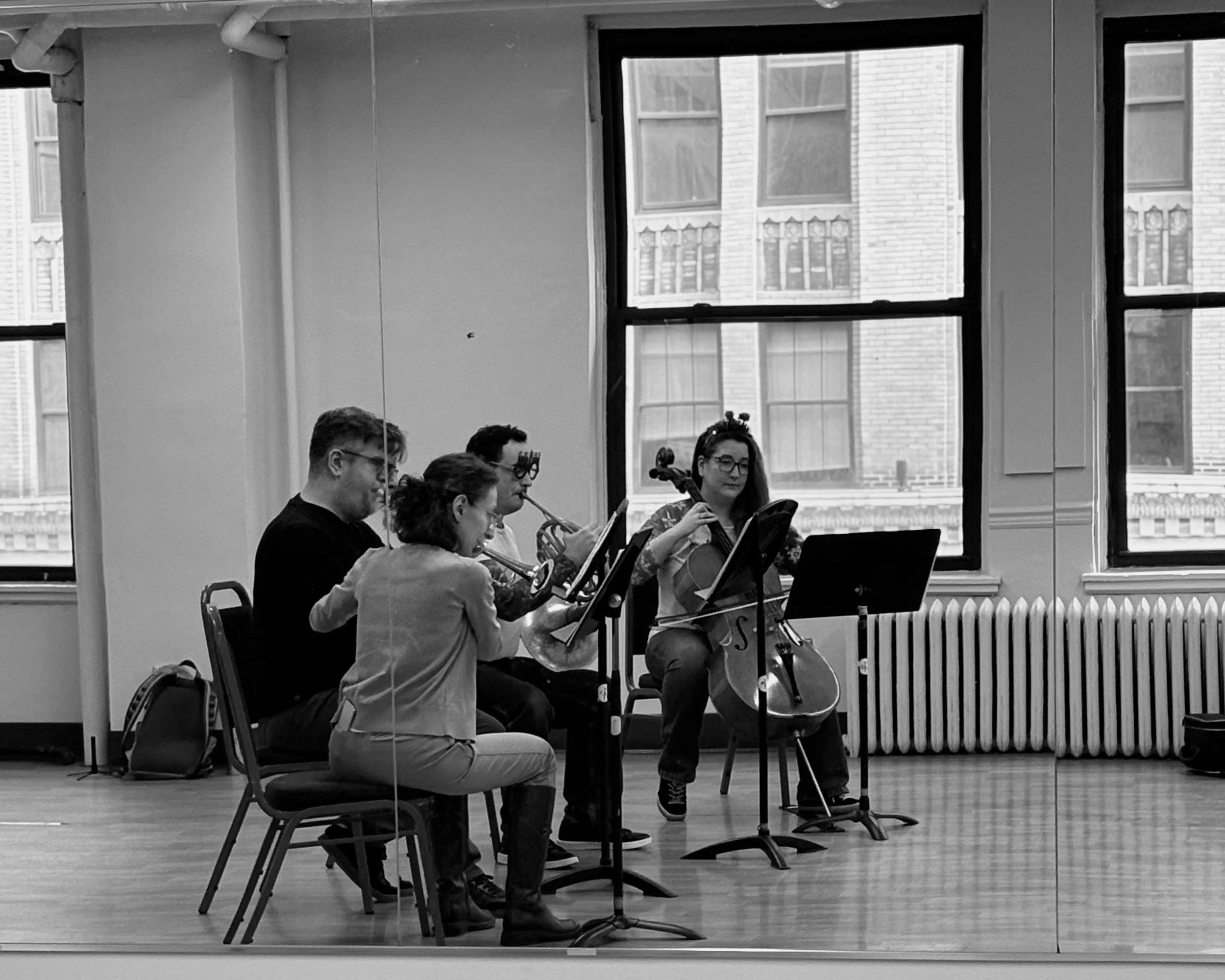 A mirror reflection of four musicians sitting in a semi circle, sight reading