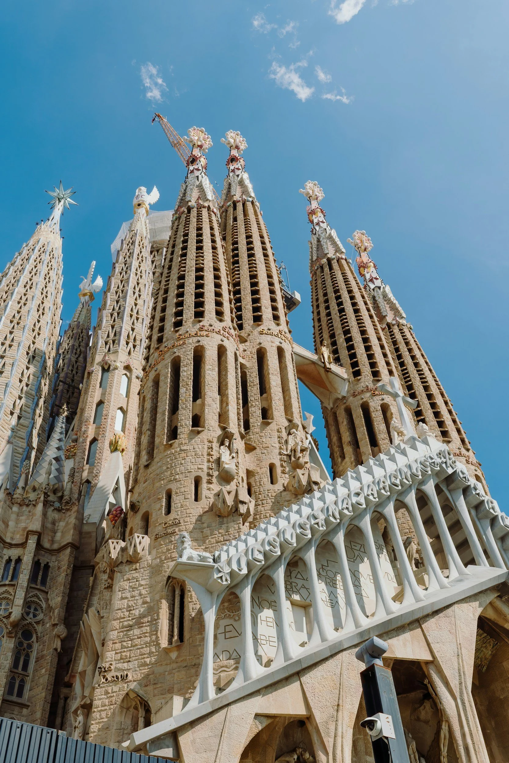 The Sagrada Familia basilica with its ornate spires and sculptures, viewed from below against a blue sky.