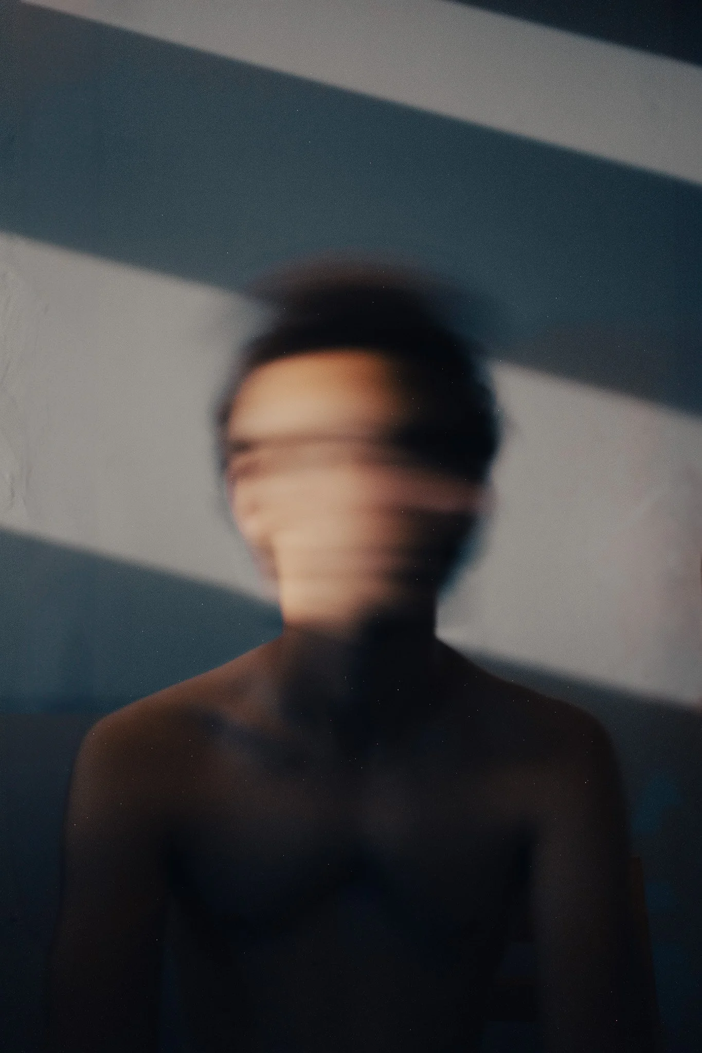 Un portrait flou d'une personne sans vêtements, avec ses yeux obscurcis par une lumière ou un reflet, dans un environnement sombre et mystérieux.