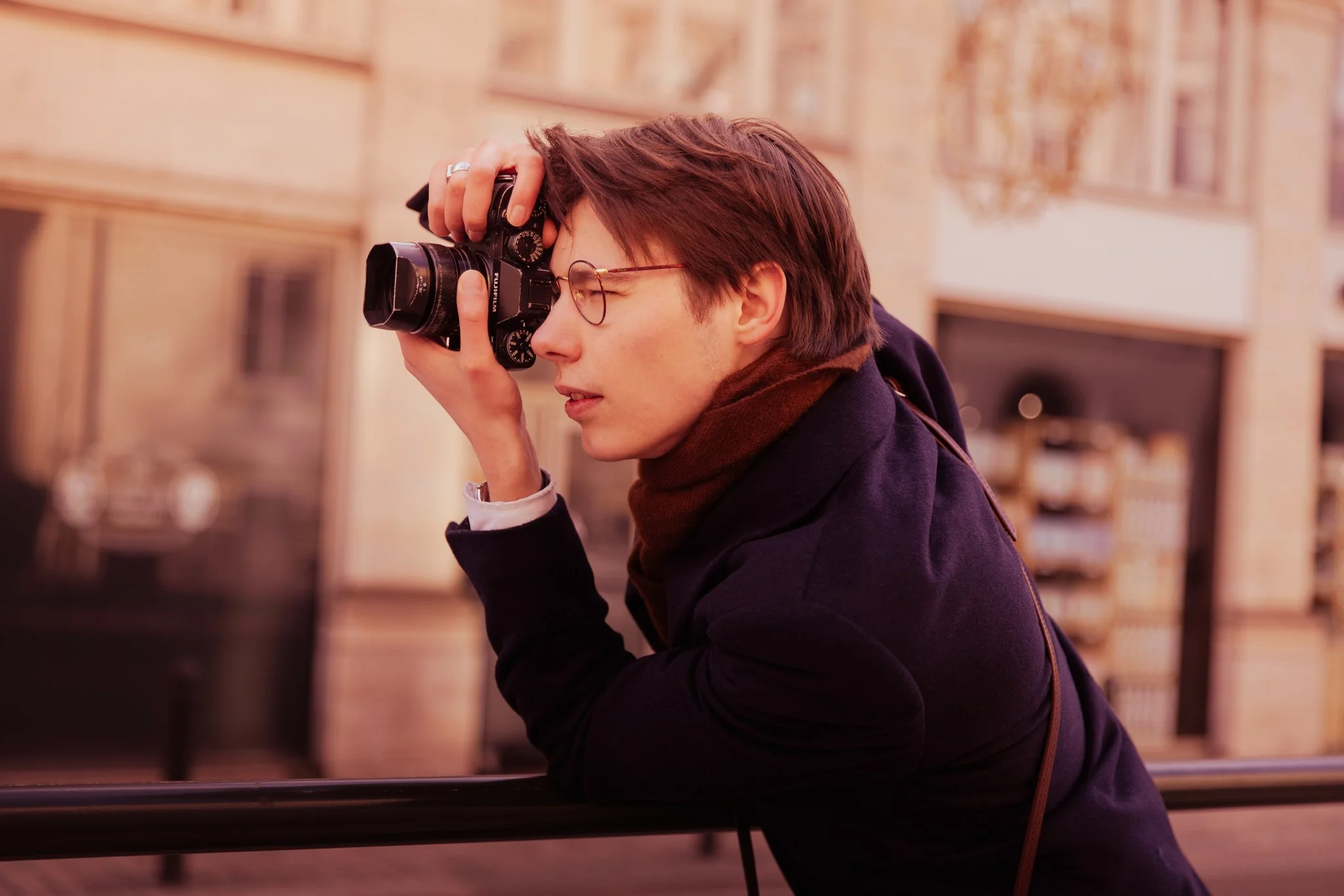 Jeune homme portant des lunettes et un manteau sombre, prenant une photo avec un appareil photo numérique, en extérieur