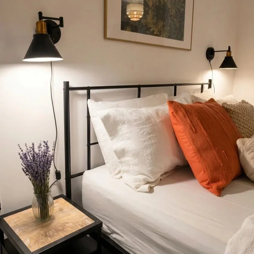 Bedroom with black iron bed frame, orange cushion and lavender bedside styling, Battersea London by Rodolfo Falcao