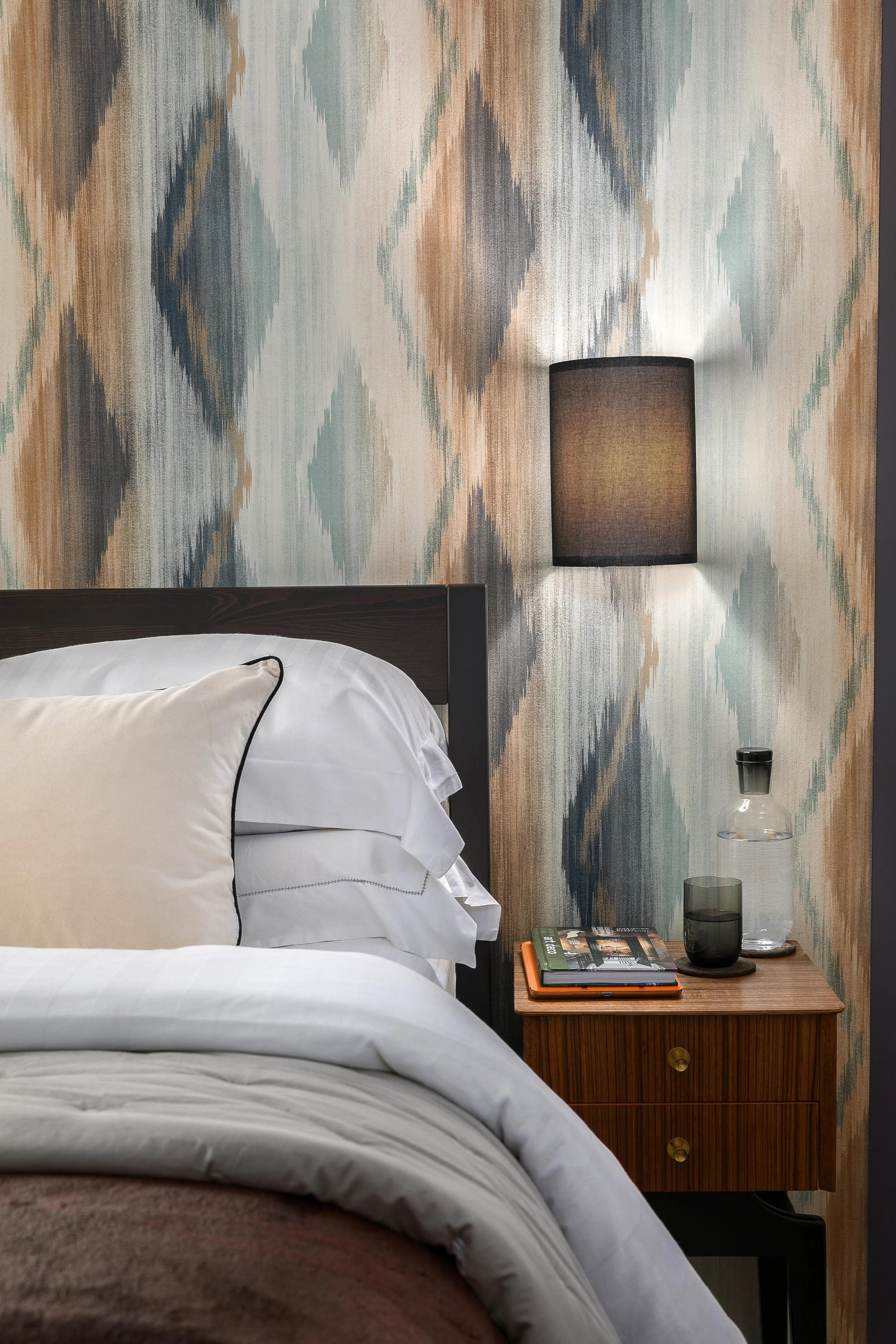 Primary bedroom detail with ikat wallpaper and walnut bedside table, Bow East London interior design by Rodolfo Falcao
