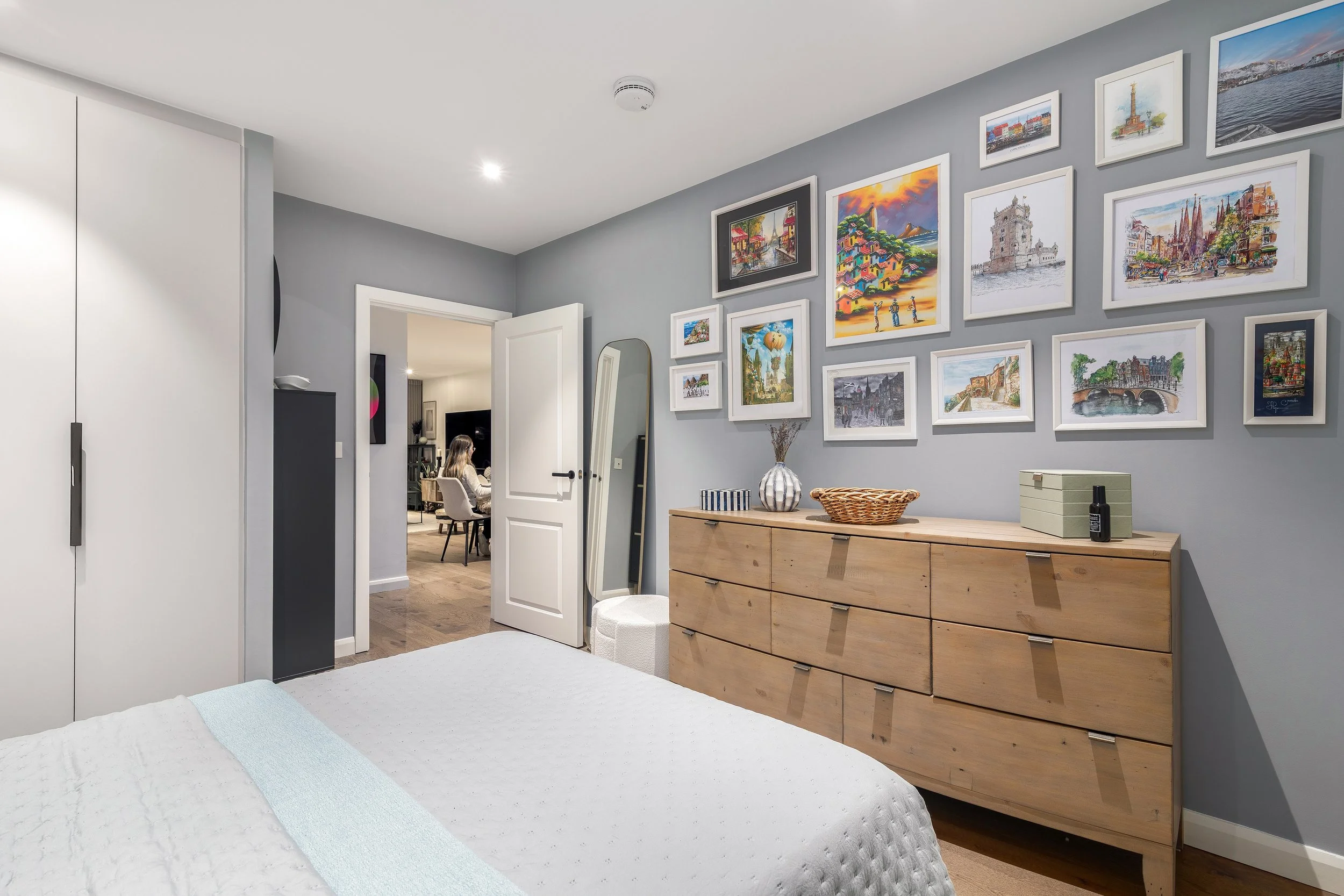 Bedroom with travel artwork gallery wall and rattan chest of drawers, Limehouse Cut East London by Rodolfo Falcao