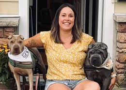 Woman sitting with two large dogs, both wearing bandanas, in front of an open door