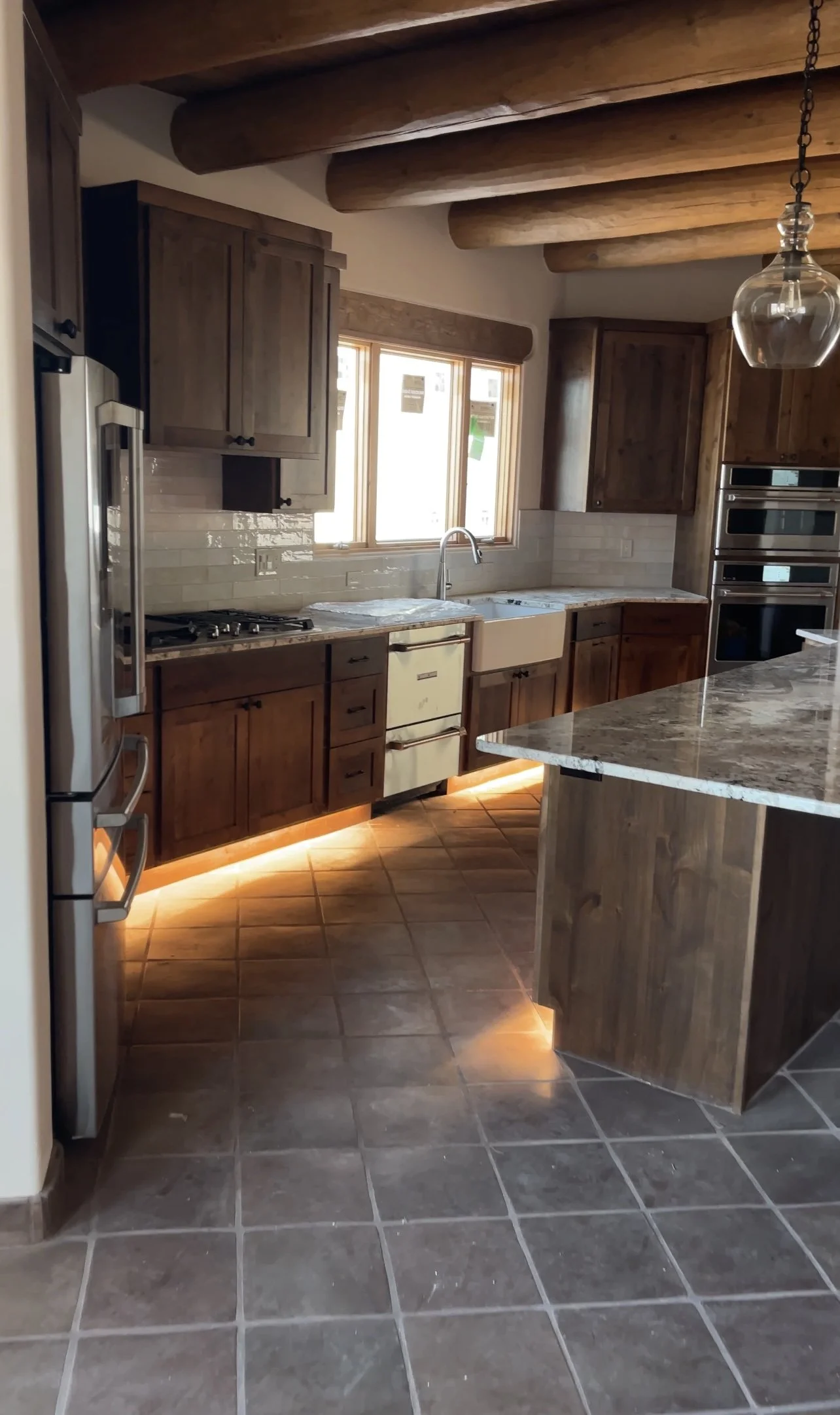 Kitchen with wooden cabinets, a window above the sink, granite countertops, pendant light, and tiled floor, with under-cabinet lighting.