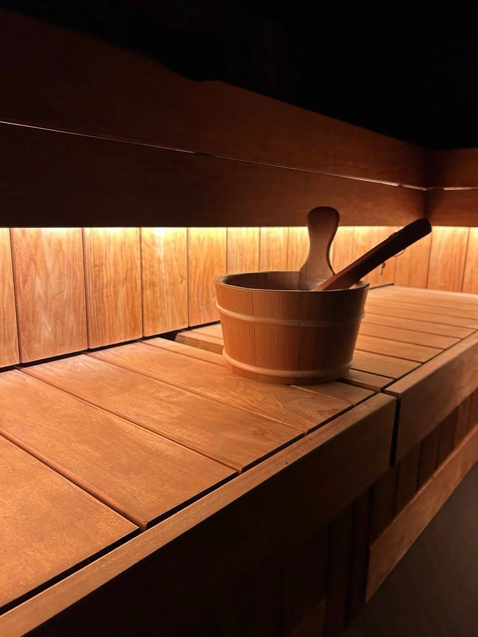 A wooden sauna interior with a bucket and two wooden utensils inside.