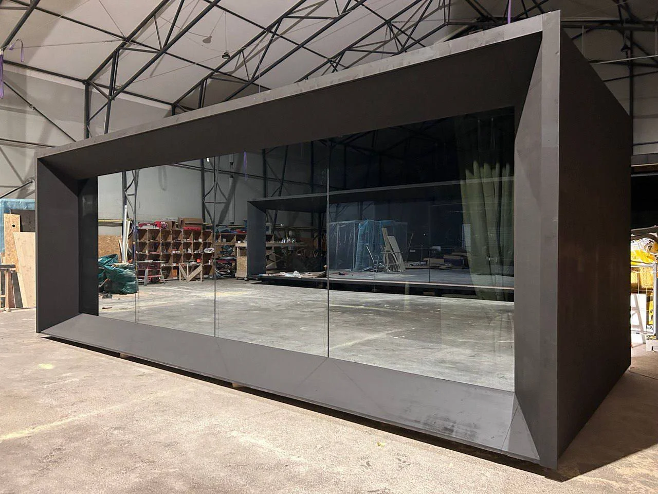 A large black rectangular structure with glass walls inside a warehouse or workshop.