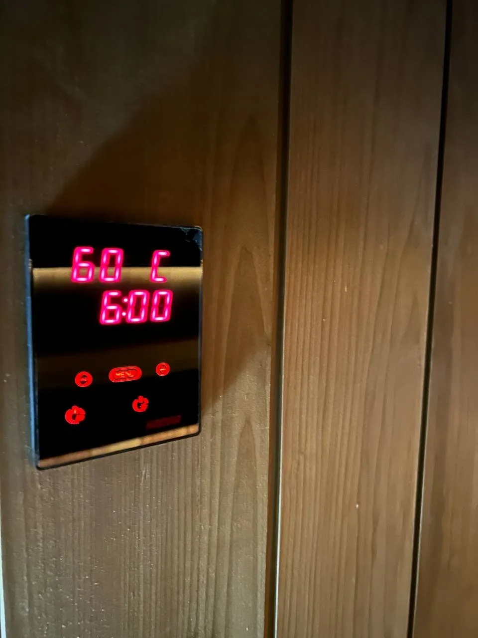 Digital control panel on wooden wall displaying 60 degrees Celsius at 6:00.