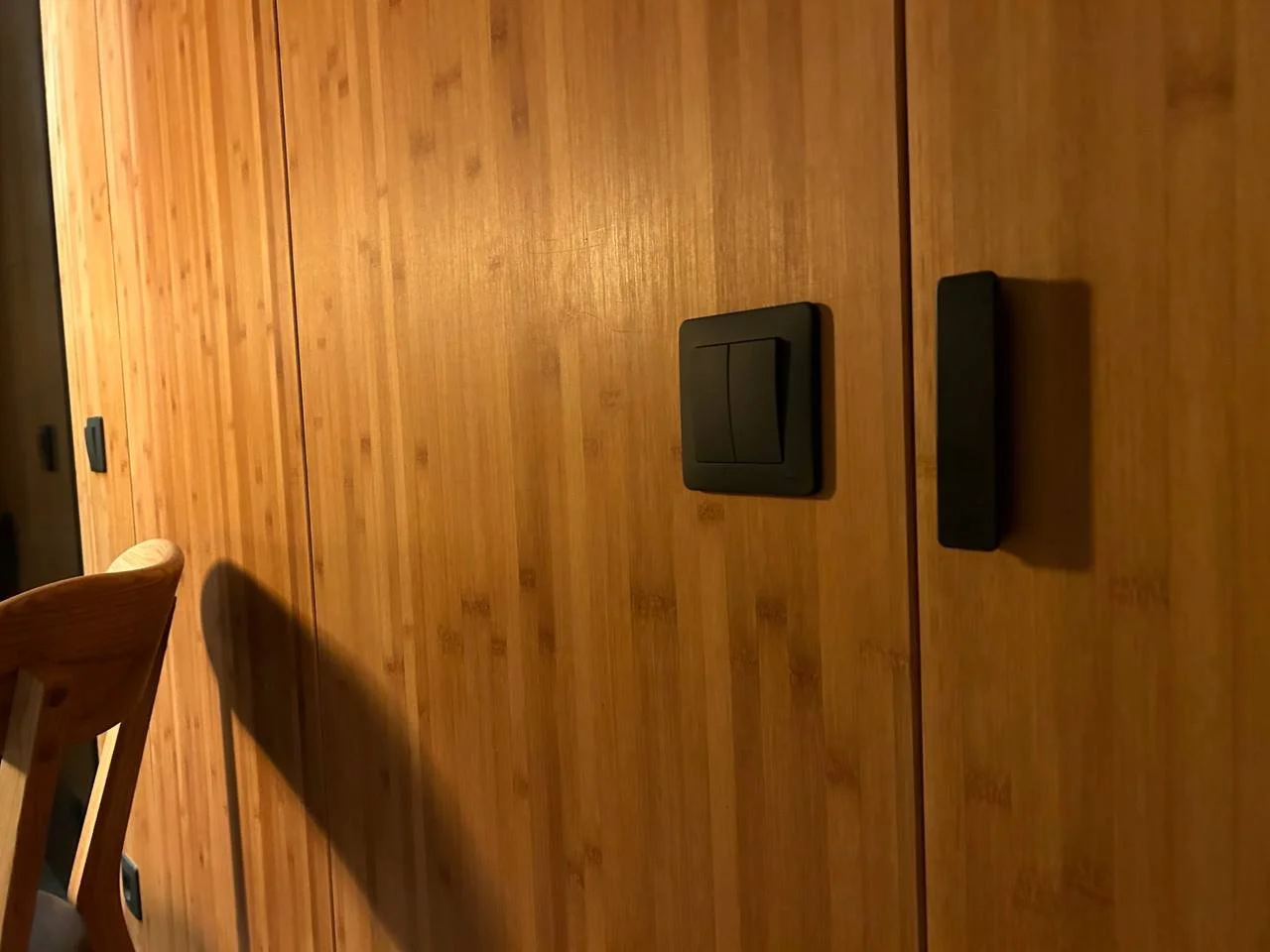 Wood-paneled wall with black switches or controls and part of a wooden chair.