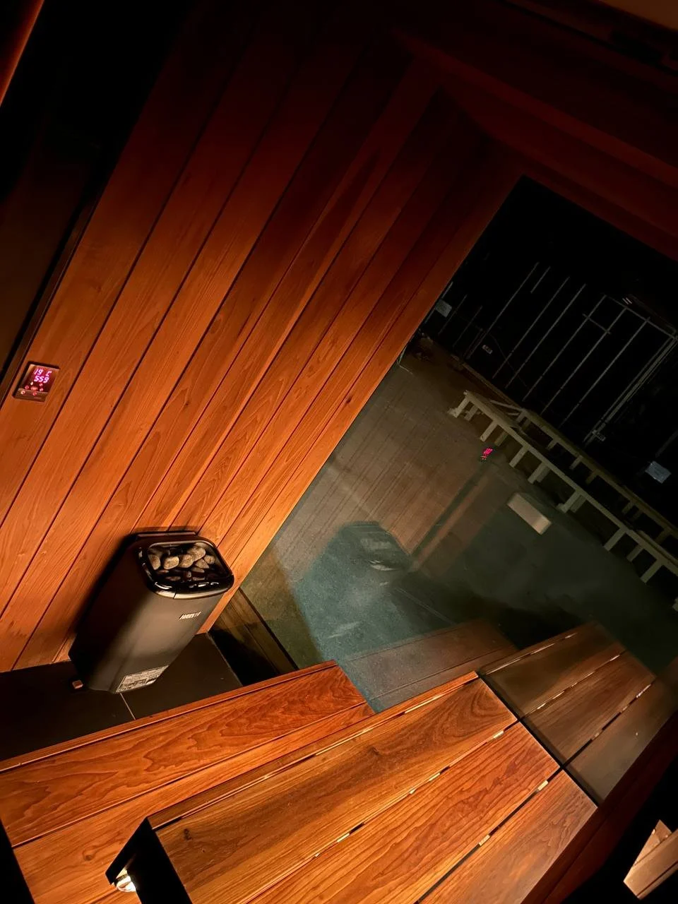 A room with wooden paneled walls, a glass window, and a small heater or fireplace with stones on top.