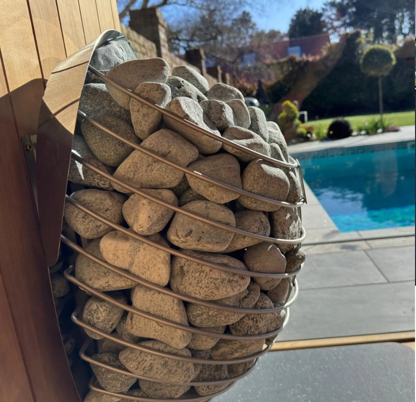 A decorative outdoor heater filled with rocks, located by a swimming pool in a backyard.