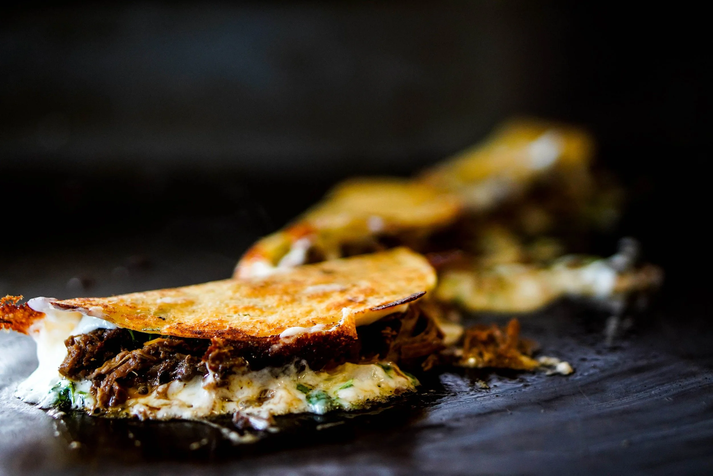 A close-up of a savory layered dish with meat, cheese, and herbs, being cooked on a black surface.
