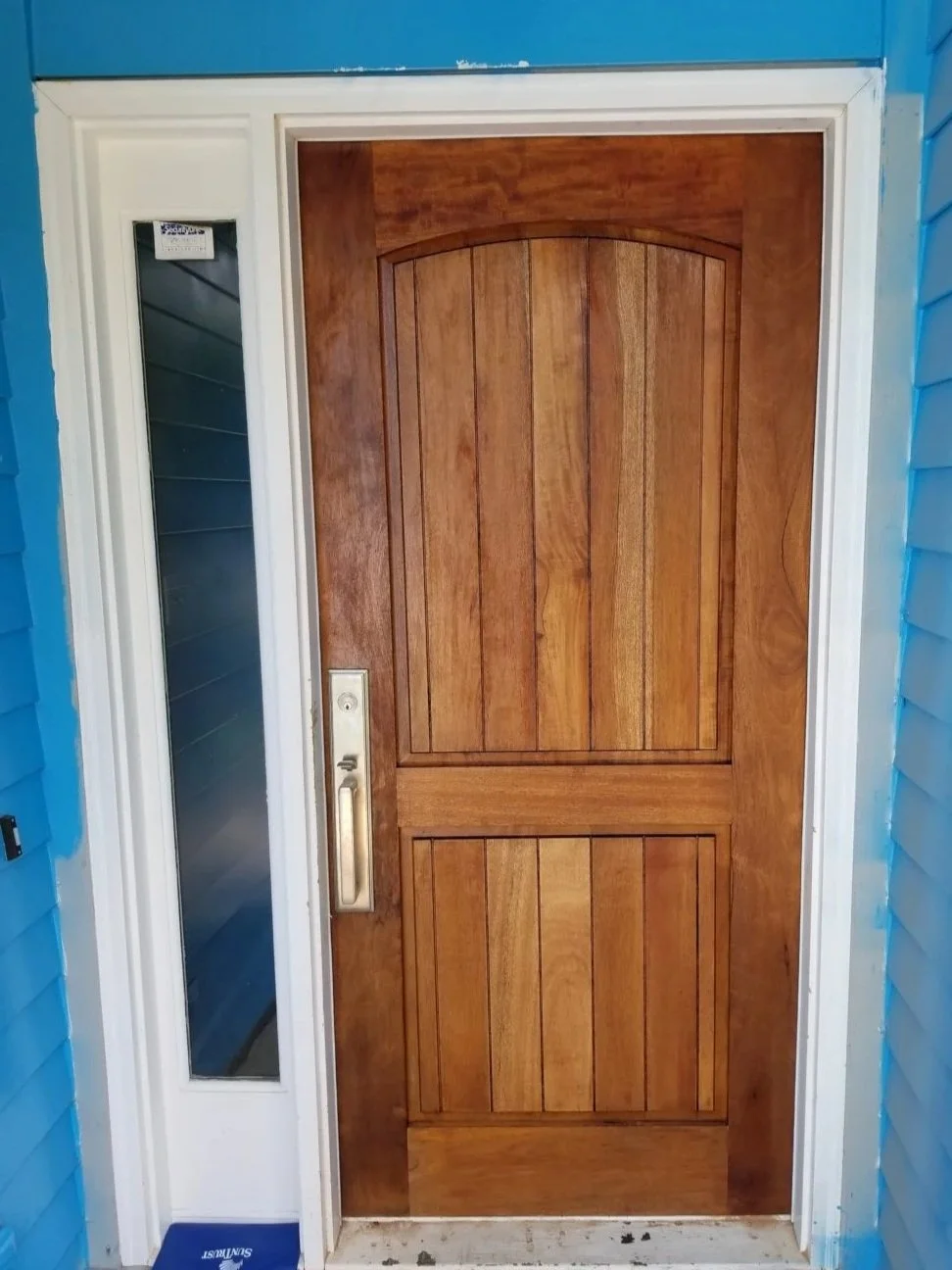 Polyurethane sealed wooden front door with a vertical rectangular window to the left, surrounded by white trim, Simpsonville, SC