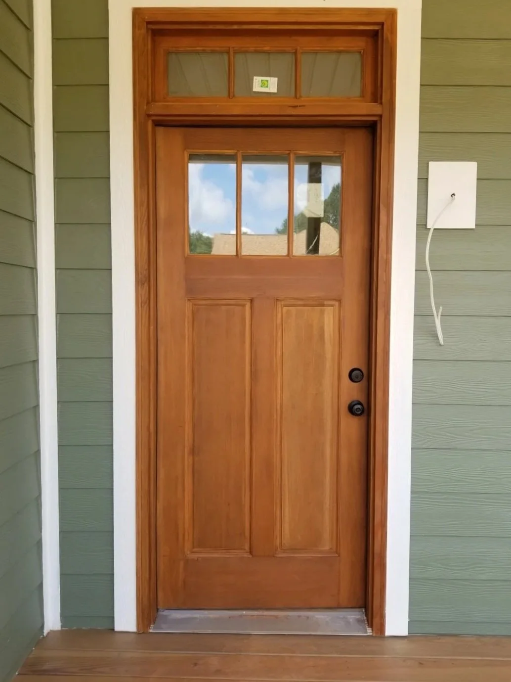 Sherwin Williams staining of a wooden front door with glass panes at the top, surrounded by a wooden frame, with green paint on the siding and white trim paint, Pickens, SC