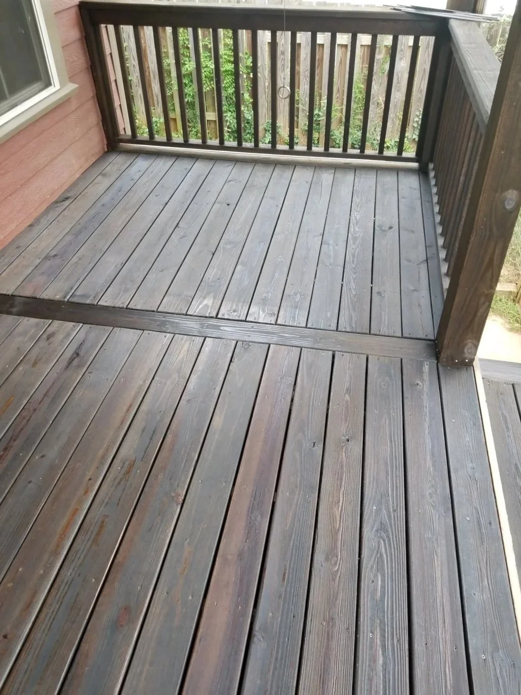 Wooden porch or deck with railing, attached to a house with red siding, overlooking greenery.