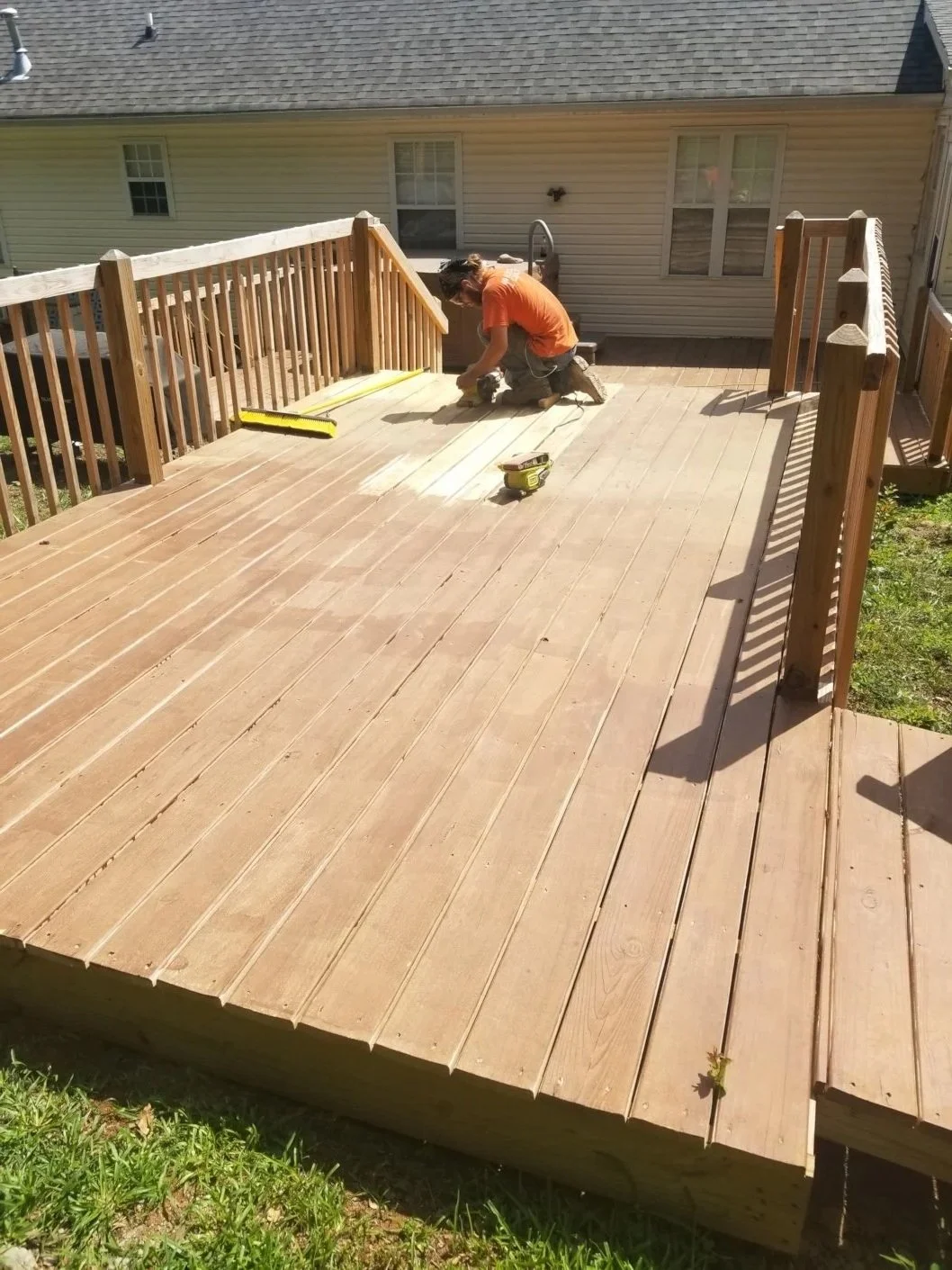 A person working on a wooden deck, measuring and installing boards, with tools on the deck and a house in the background.