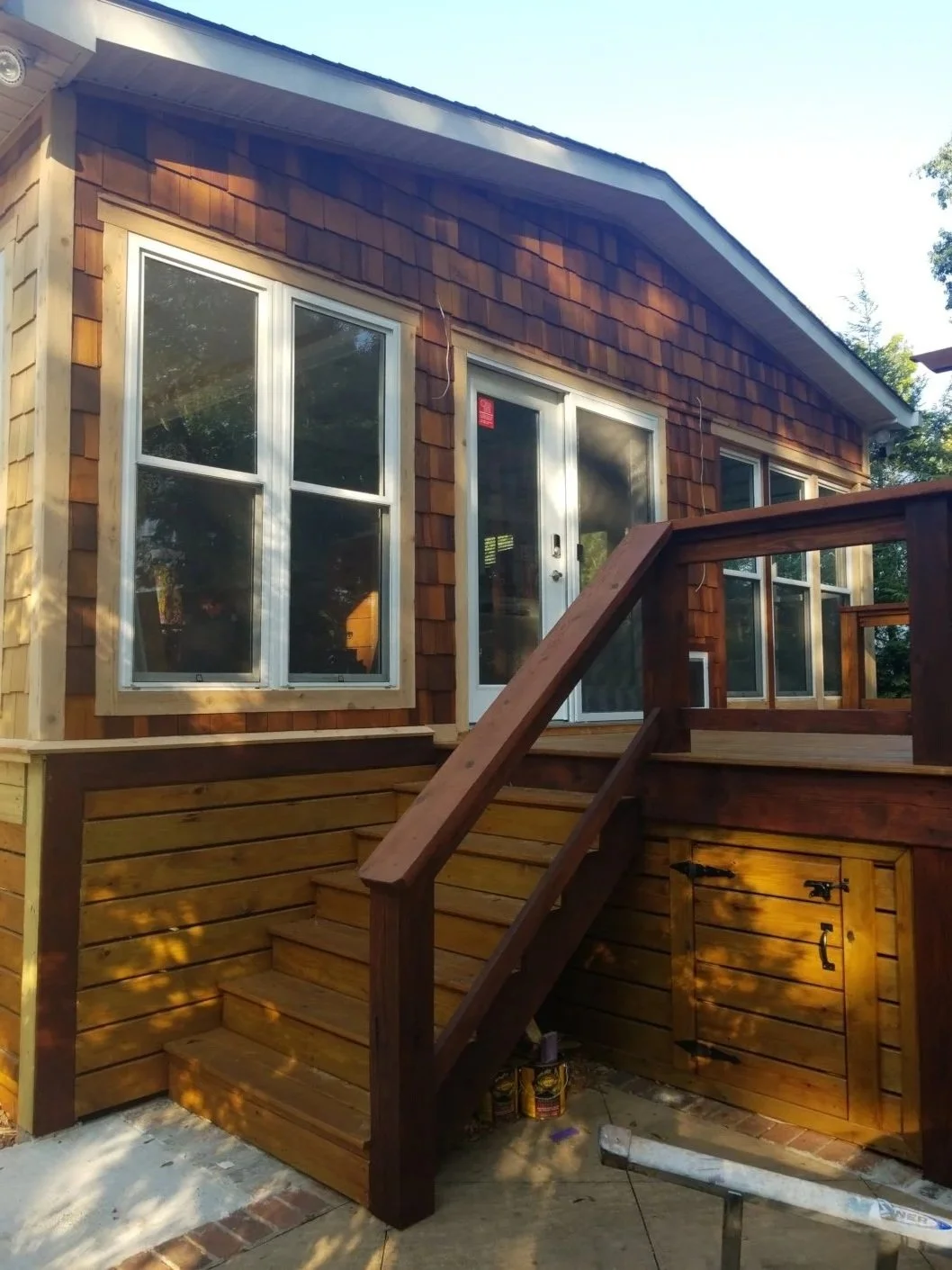 Newly constructed wooden deck with stairs leading to a house with shingle siding and white-framed windows, during daytime.