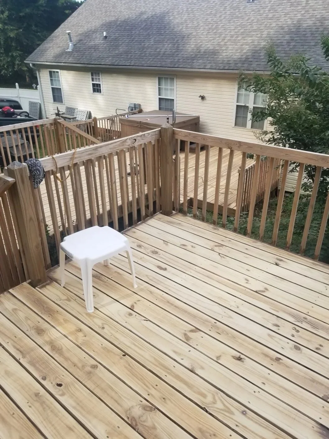 Wooden deck attached to a house with a white plastic stool on it and a view of neighboring houses and trees.