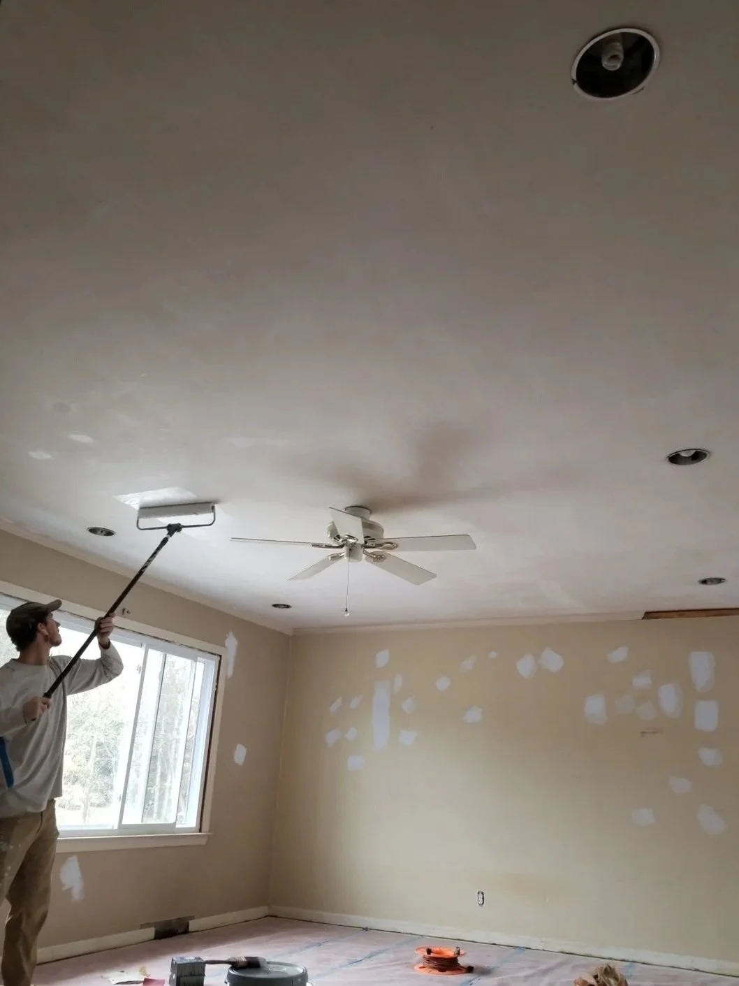 Person painting ceiling in a room with drywall patches on walls.