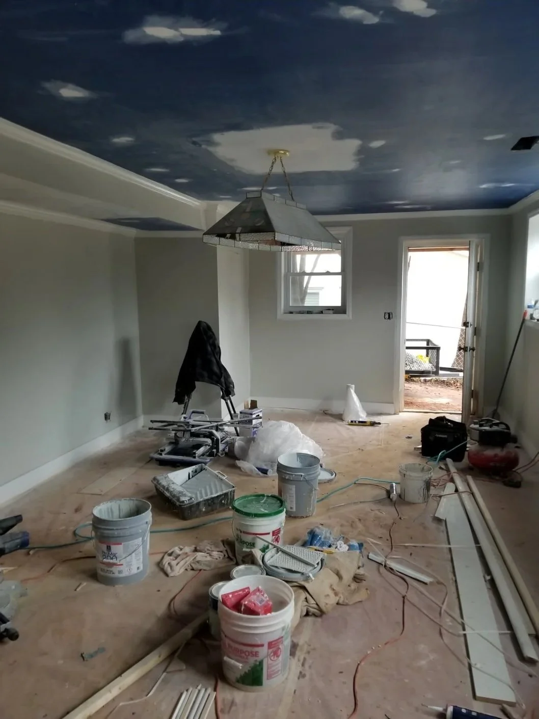 Room under renovation with a painted sky ceiling, construction tools, and supplies scattered on the unfinished floor.