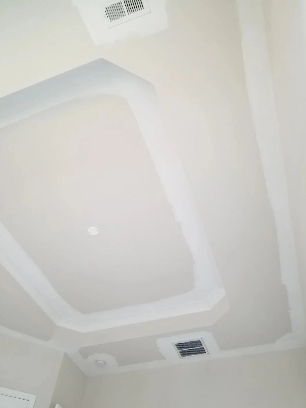 Ceiling with vent, smoke detector, and recessed lighting in a room with white walls.
