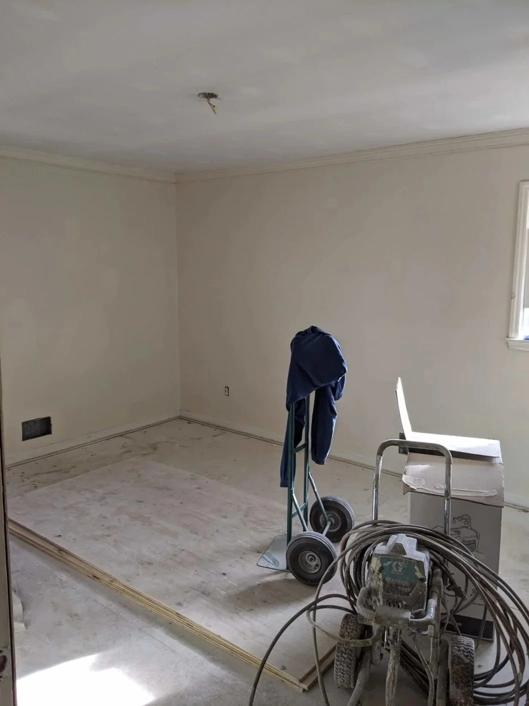 Empty room under renovation with construction tools, a chair, a dolly with a cloth, and a drop cloth on the floor.