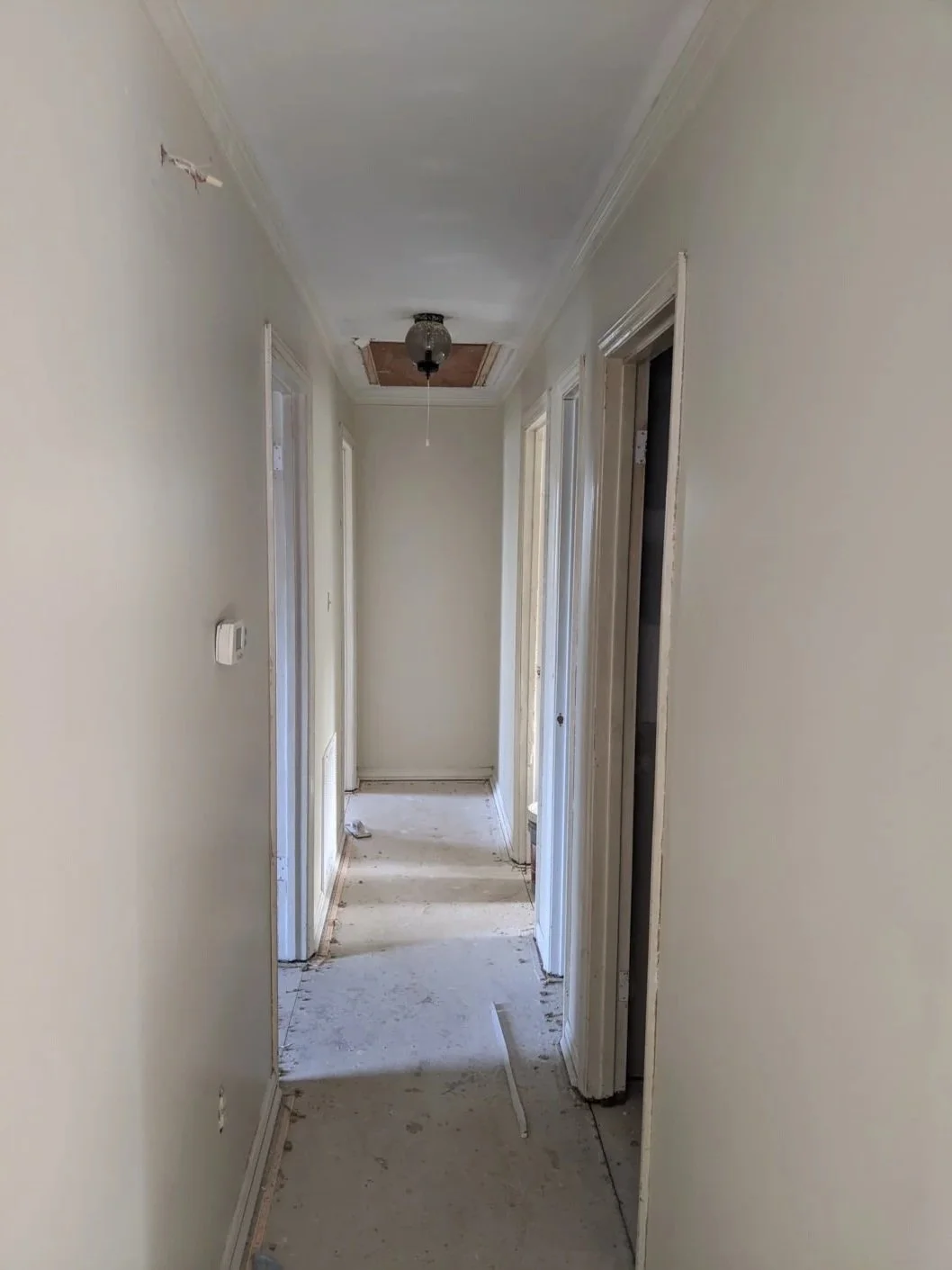 Empty hallway in a house under renovation with unfinished walls, a missing ceiling light fixture, and construction debris on the floor.