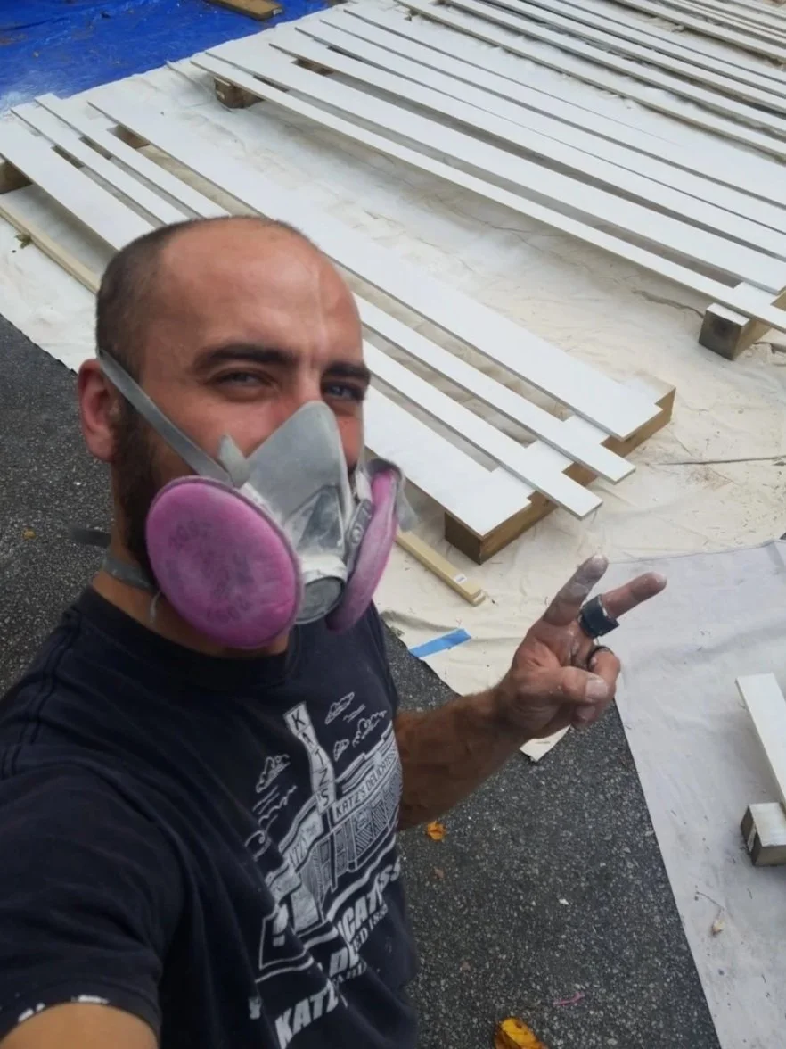Man taking a selfie while wearing a respirator mask, with wooden planks and covered surface in the background.