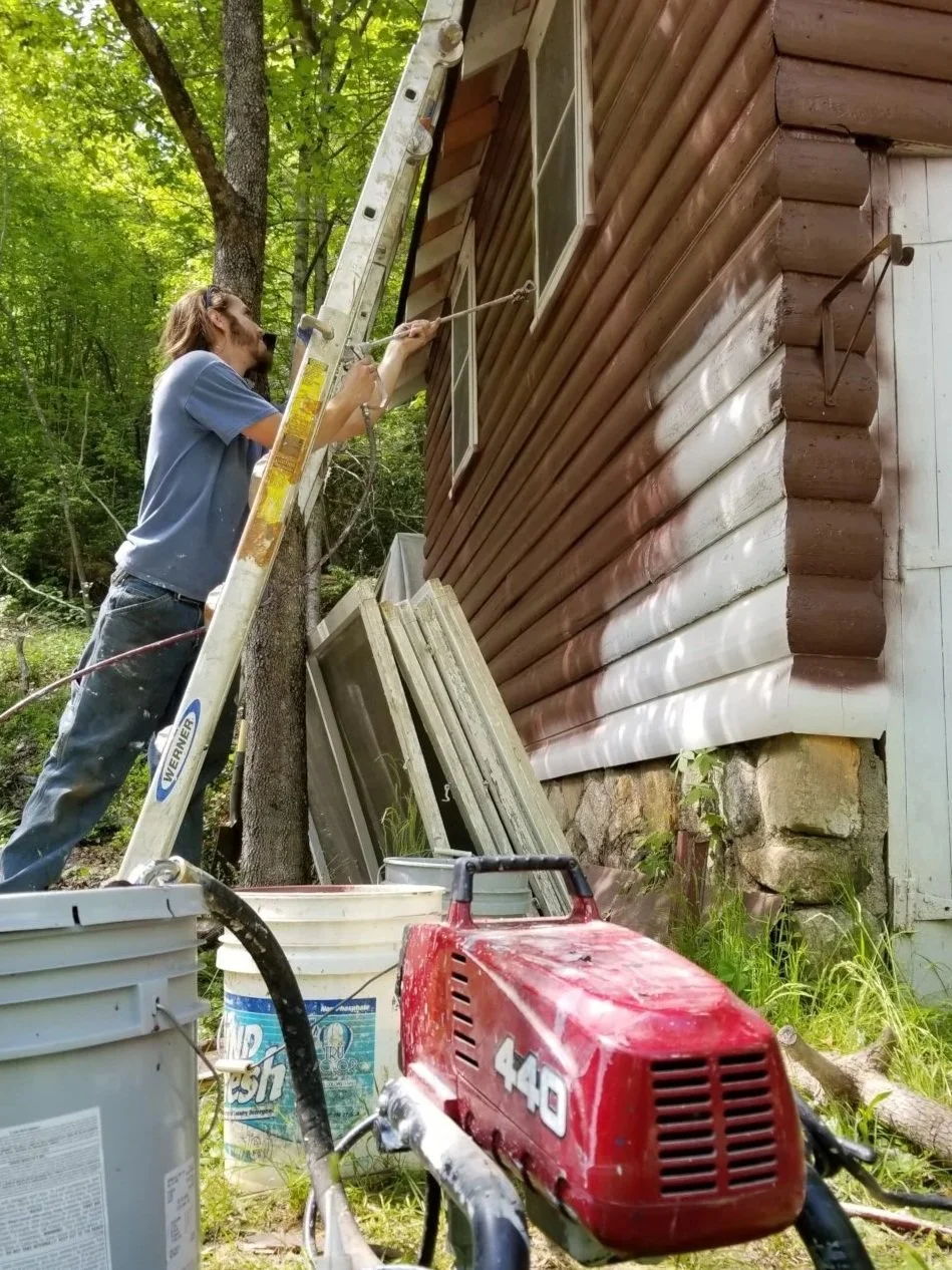 A man on a ladder pressure washing the exterior wall of a wooden house.