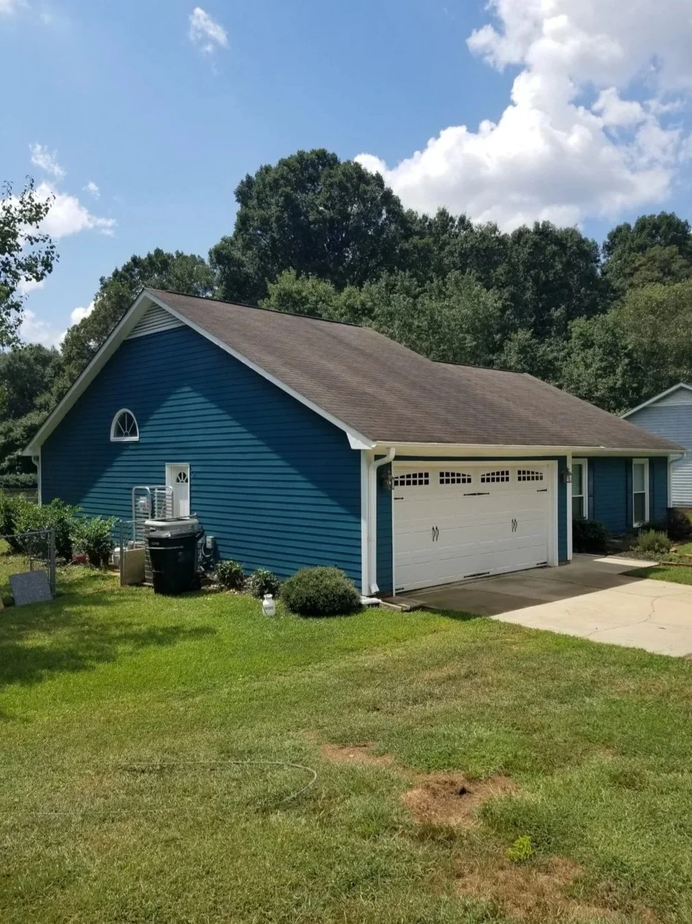 A blue garage with a white door, green lawn, and trees in the background.
