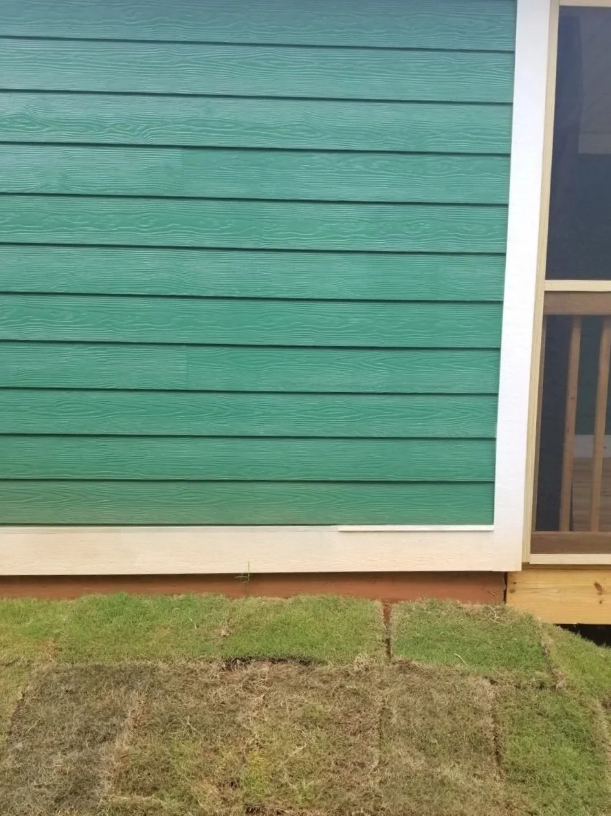 Close-up of a house's exterior with colored siding and a small patch of grass in front.