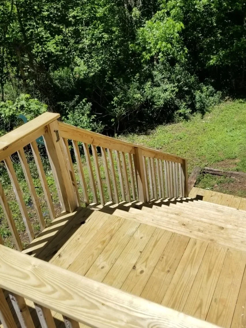 Wooden staircase leading down to a grassy yard with trees in the background.